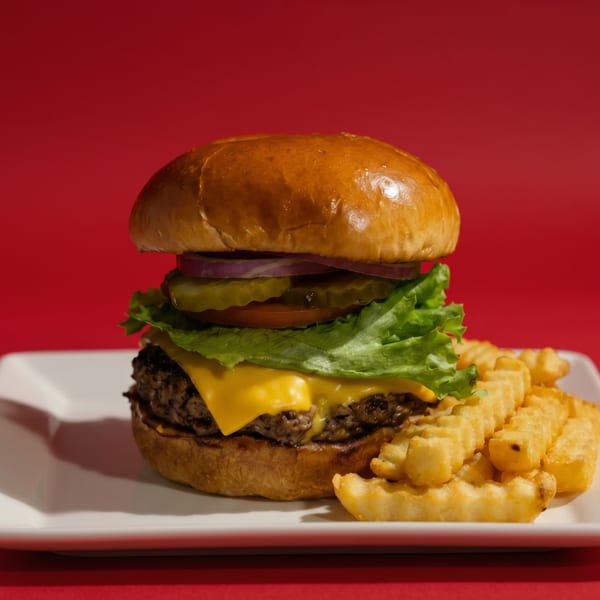 Cheeseburger with lettuce, tomato, onion, and pickles, served with crinkle-cut fries on a white plate.